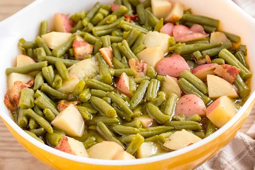 Green beans with potatoes and bacon in yellow bowl.