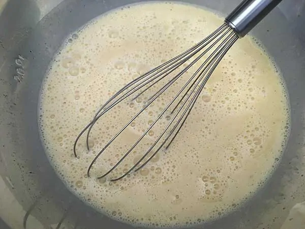 Eggs and milk in mixing bowl with whisk.