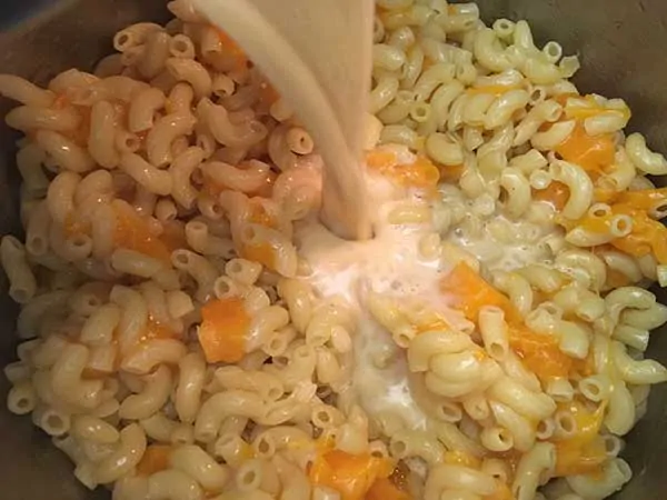 Egg mixture pouring over pasta and cheese.