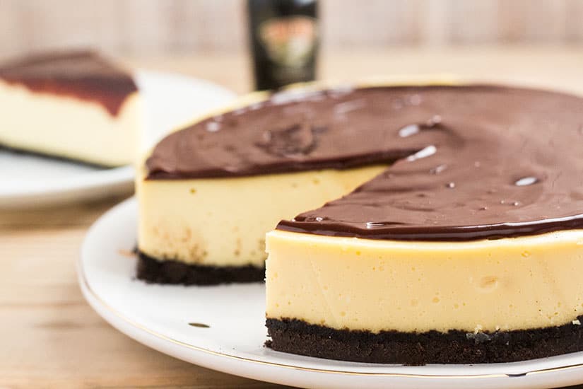 Whole cheesecake, covered in chocolate, with one slice removed.