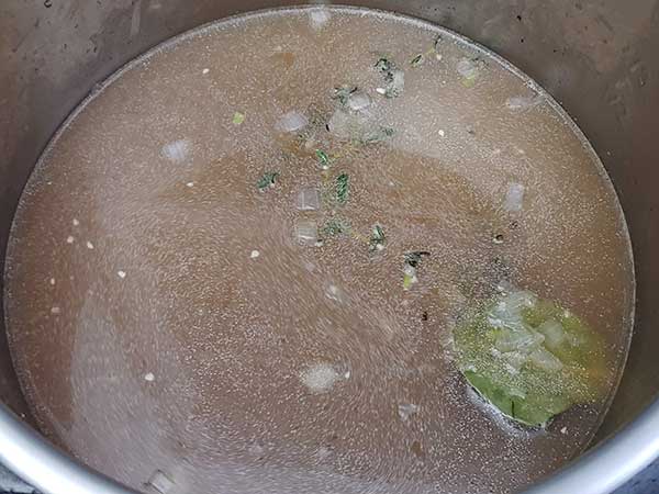 Chicken stock in pot with aromatics.