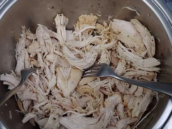 Shredding chicken in bowl with two forks.