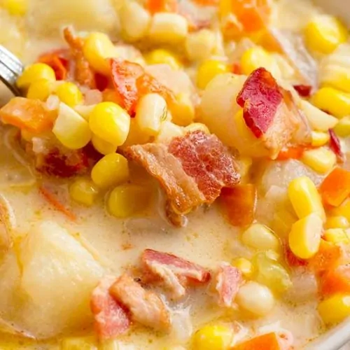 Close up of corn chowder in white bowl with spoon.