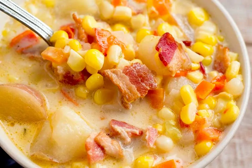 Close up of corn chowder in white bowl with spoon.