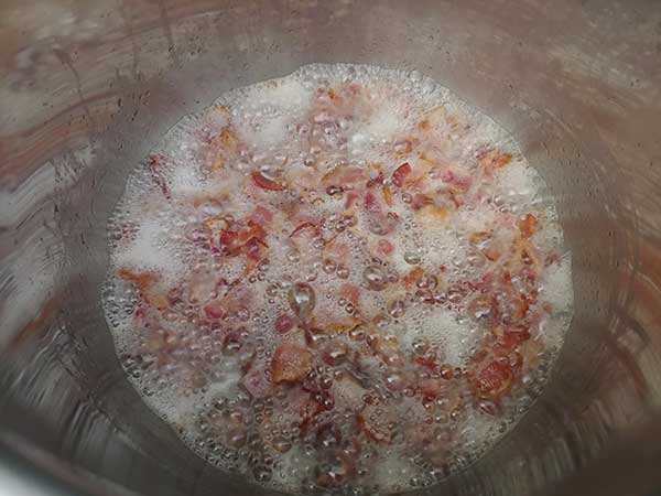 Bacon pieces cooking in pot.