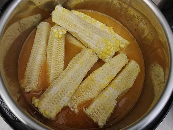 Corn cobs on to of potatoes in broth.