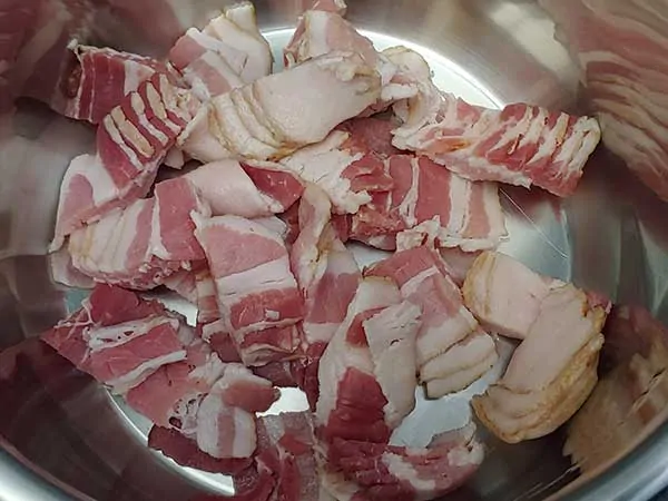 Uncooked bacon pieces in pot.