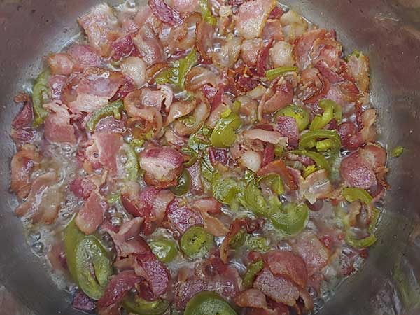 SautÃ©ing bacon pieces with sliced jalapeÃ±os.