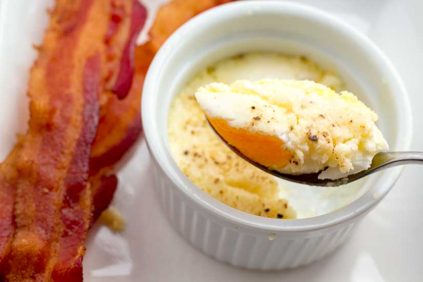 Spoonful of baked egg in ramekin with bacon on the side.