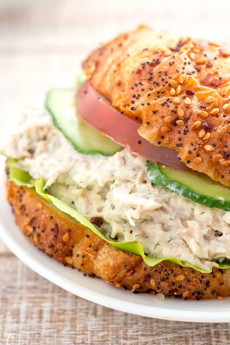 Chicken salad sandwich on croissant with tomato and cucumbers.