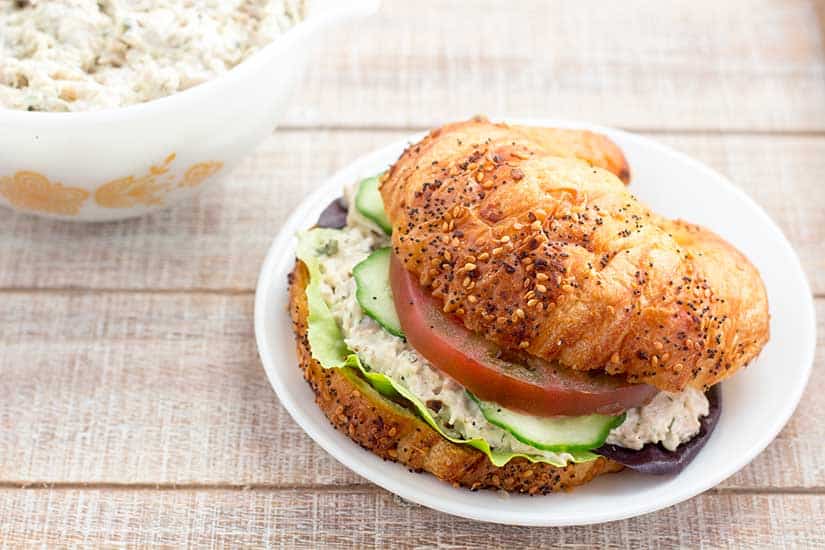 Chicken salad sandwich on croissant with tomato and cucumbers.