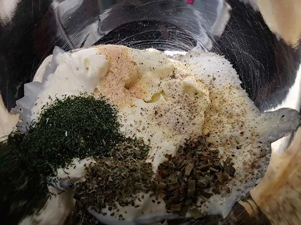Mayonaise and herbs in mixing bowl.