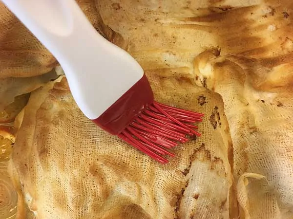 Basting turkey through cheesecloth with basting brush.