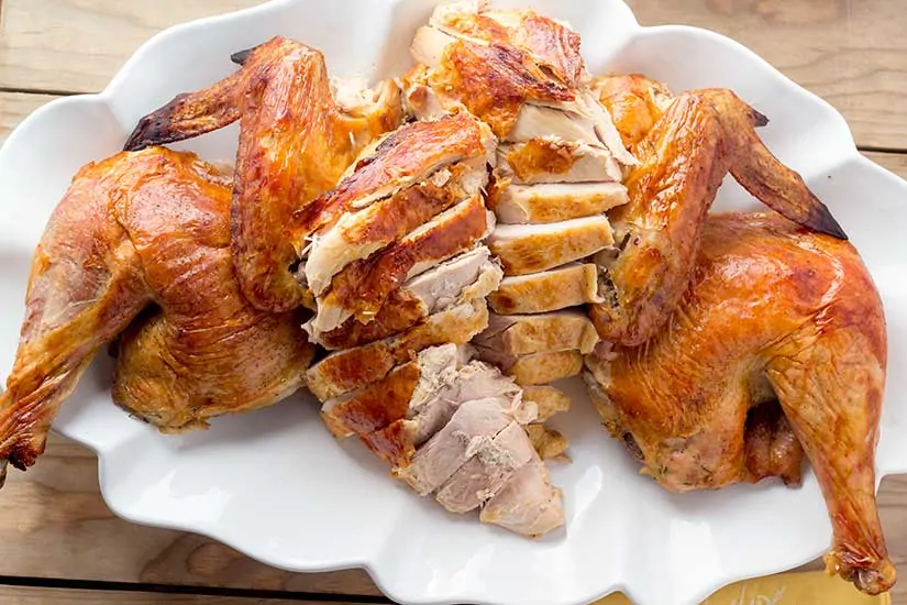Spatchcock turkey cut up on white serving platter.