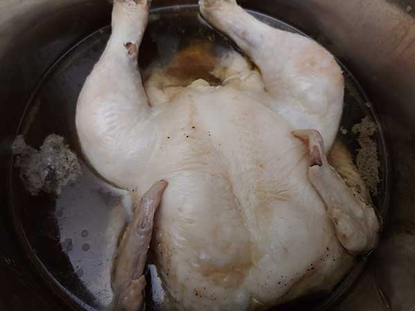 Whole cooked chicken in pot with broth.