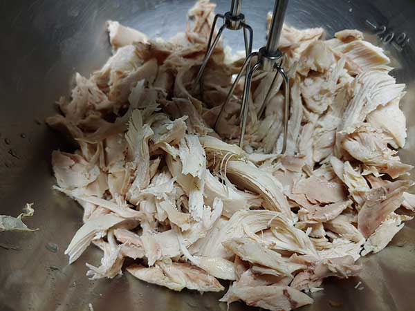 Chicken meat in mixing bowl with hand mixer.