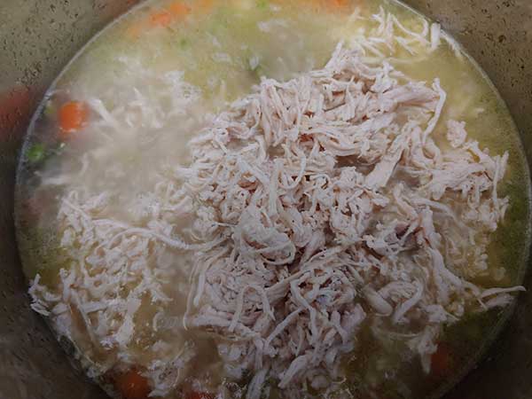 Shredded chicken on top of cooked soup.