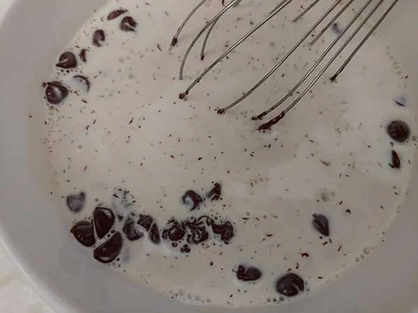 Mixing chocolate chips and heavy cream with whisk in bowl.