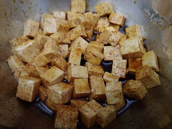 Small cubes of tofu marinating in mixing bowl.