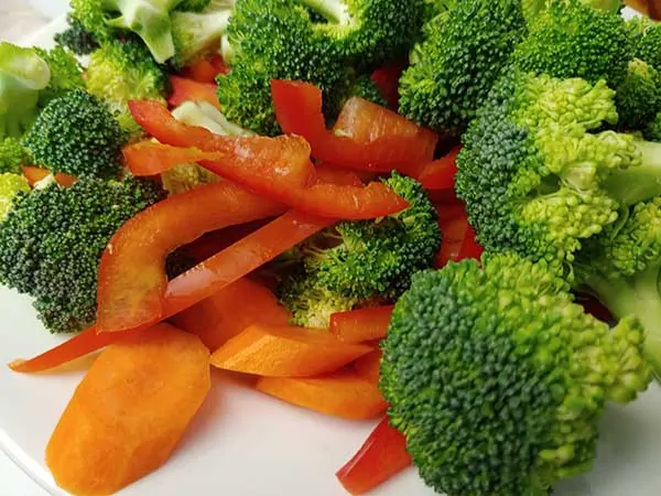 Prepped carrots, red bell peppers, and broccoli florets on white plate.