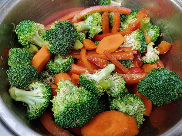 Broccoli, carrots, and red bell peppers marinating in mixing bowl.