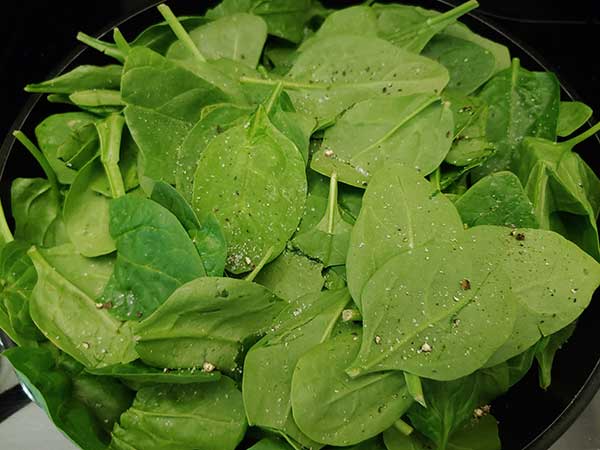 Raw baby spinach in pan seasoned with salt and pepper.