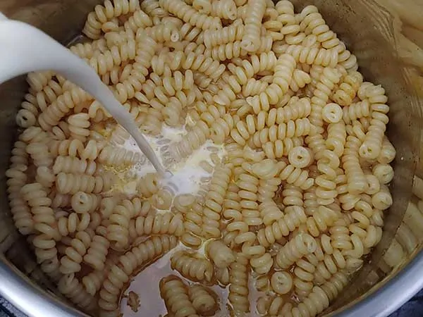 Pouring evaporated milk over cooked pasta.
