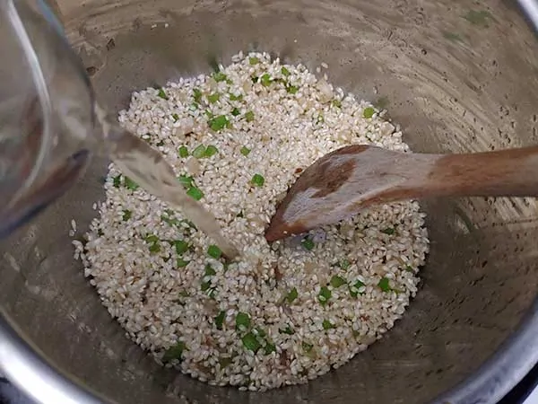 Pouring white wine into pot with uncooked risotto rice.