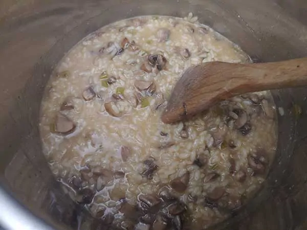 Mixing mushroom risotto in Instant Pot with wooden spatula.