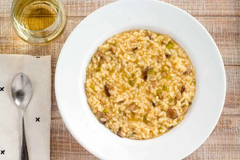 Instant Pot mushroom risotto in white bowl with glass of wine.