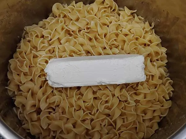 Block of cream cheese on top of cooked egg noodles.