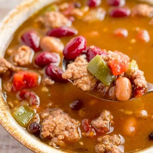 Spoonful of turkey chili with tan-rimmed bowl.