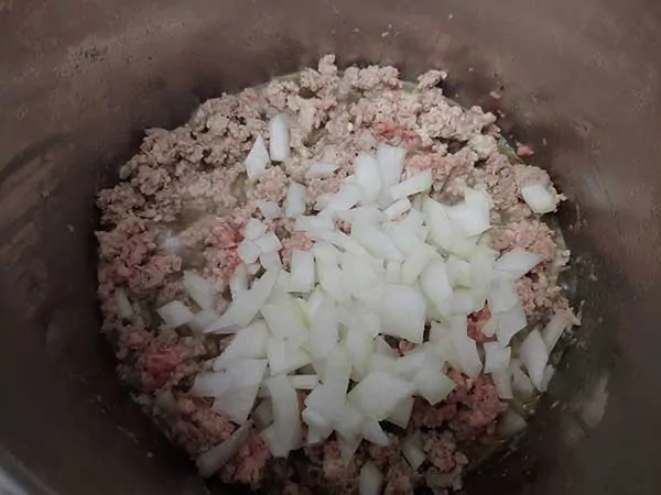 Browning ground turkey in Instant Pot topped with diced onions.