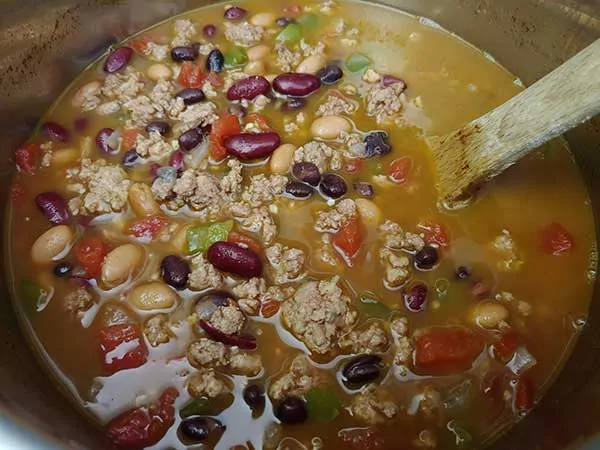 Cooked chili in pot with wooden spoon.