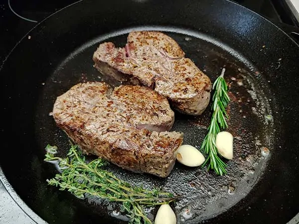 Two filet mignons in cast iron skillet with garlic, thyme, and rosemary.