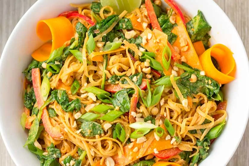 Thai Noodle Salad with curls of carrot and sliced limes in white bowl.