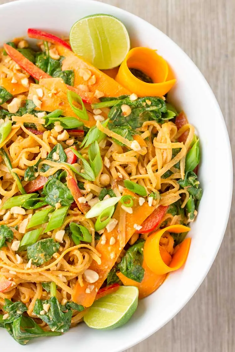 Thai Noodle Salad with curls of carrot and sliced limes in white bowl.