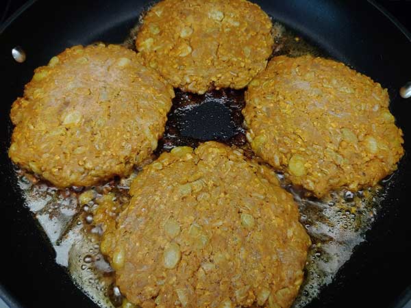 Four frozen bean burger patties frying in nonstick pan.