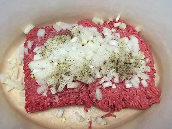 Uncooked ground beef in Dutch oven, topped with diced onions, salt, and pepper.