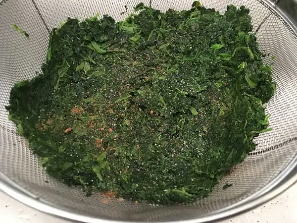 Defrosted chopped spinach in fine mesh strainer, seasoned with salt and nutmeg.
