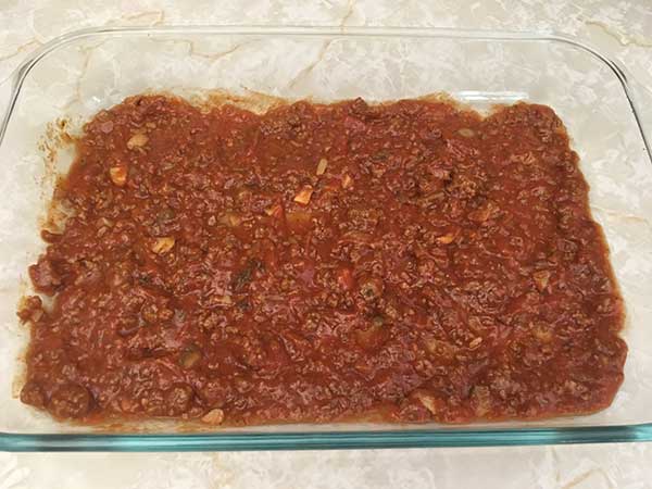 One layer of tomato sauce in casserole dish.