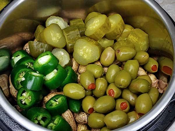 Pickles, jalapenos, and olives on top of peanuts in Instant Pot.