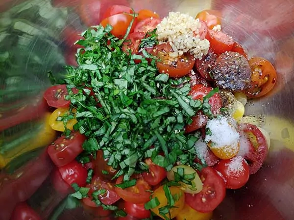 Sliced grape tomatoes, chiffonade basil, and garlic in mixing bowl.