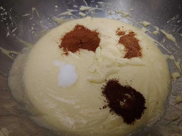 Butter, sugar, and eggs mixture in mixing bowl topped with spices.