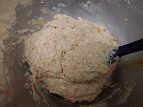 Carrot cake batter in mixing bowl with rubber spatula.