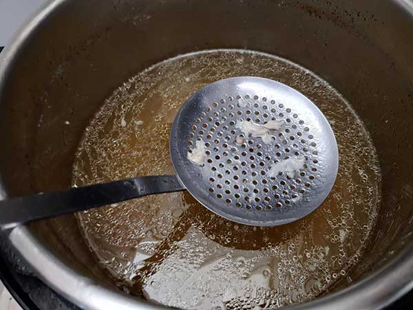 Using slotted spoon to strain chicken broth.