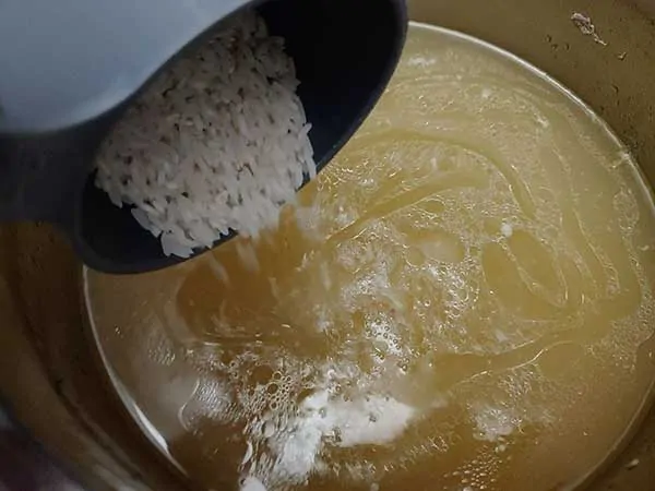 Pouring uncooked rice into chicken broth.