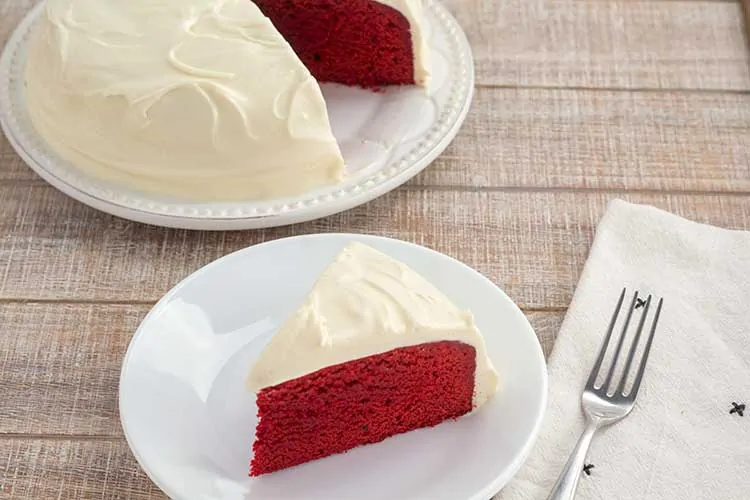 Slice of Instant Pot red velvet cake on white plate with cake in background.