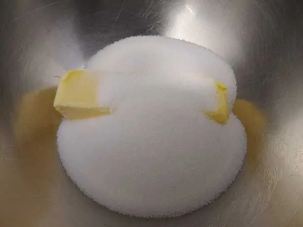 Stick of softened butter in mixing bowl with sugar on top.
