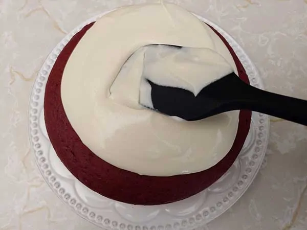 Icing cake on white plate with rubber spatula.